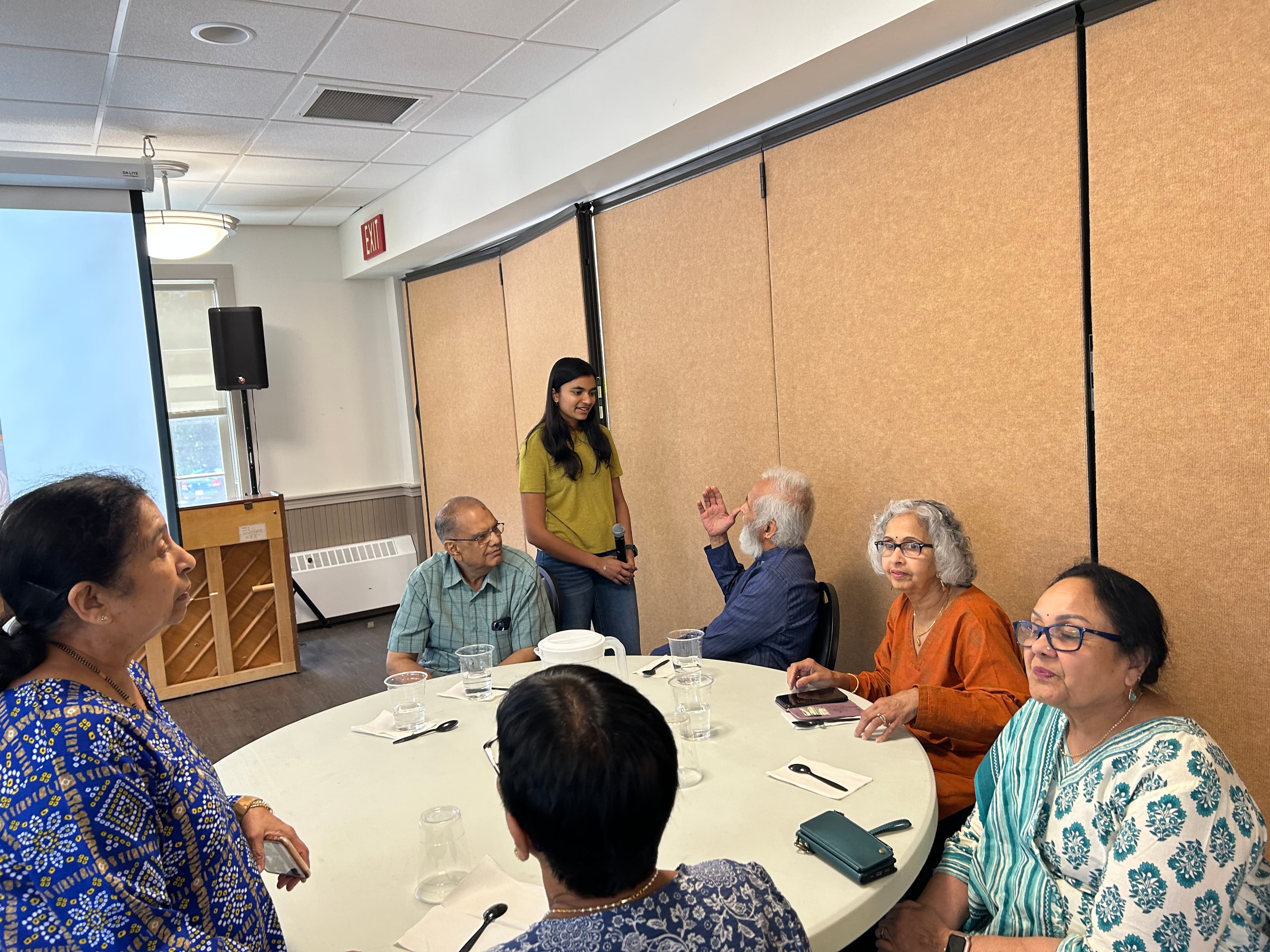 A senior gestures while speaking as Naaisha listens during an AI For Seniors workshop.